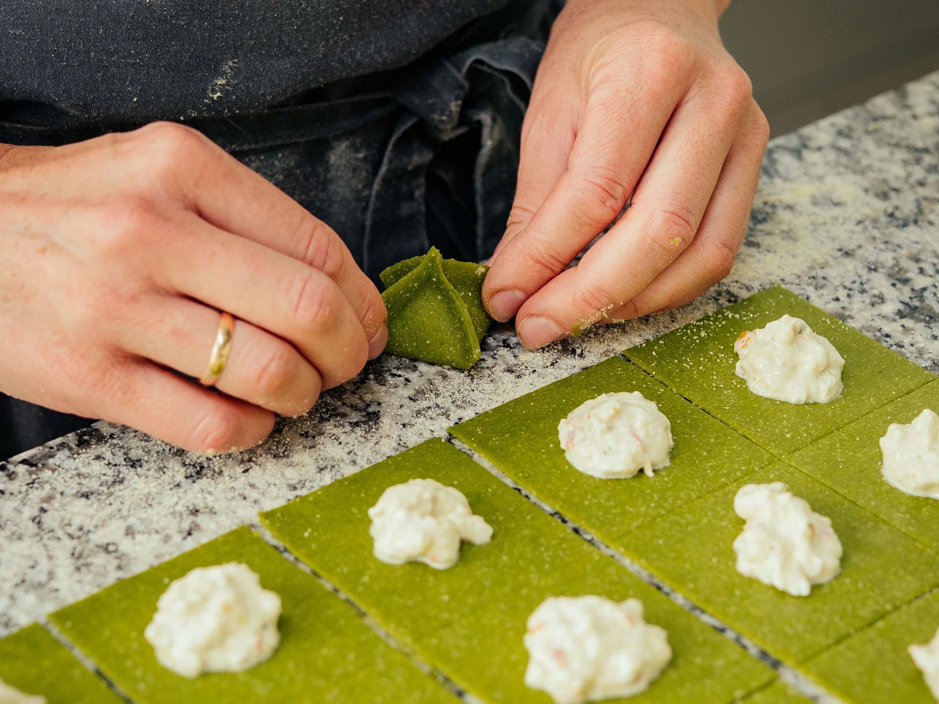 Hände formen grüne Teigquadrate mit weißer Füllung zu Pasta