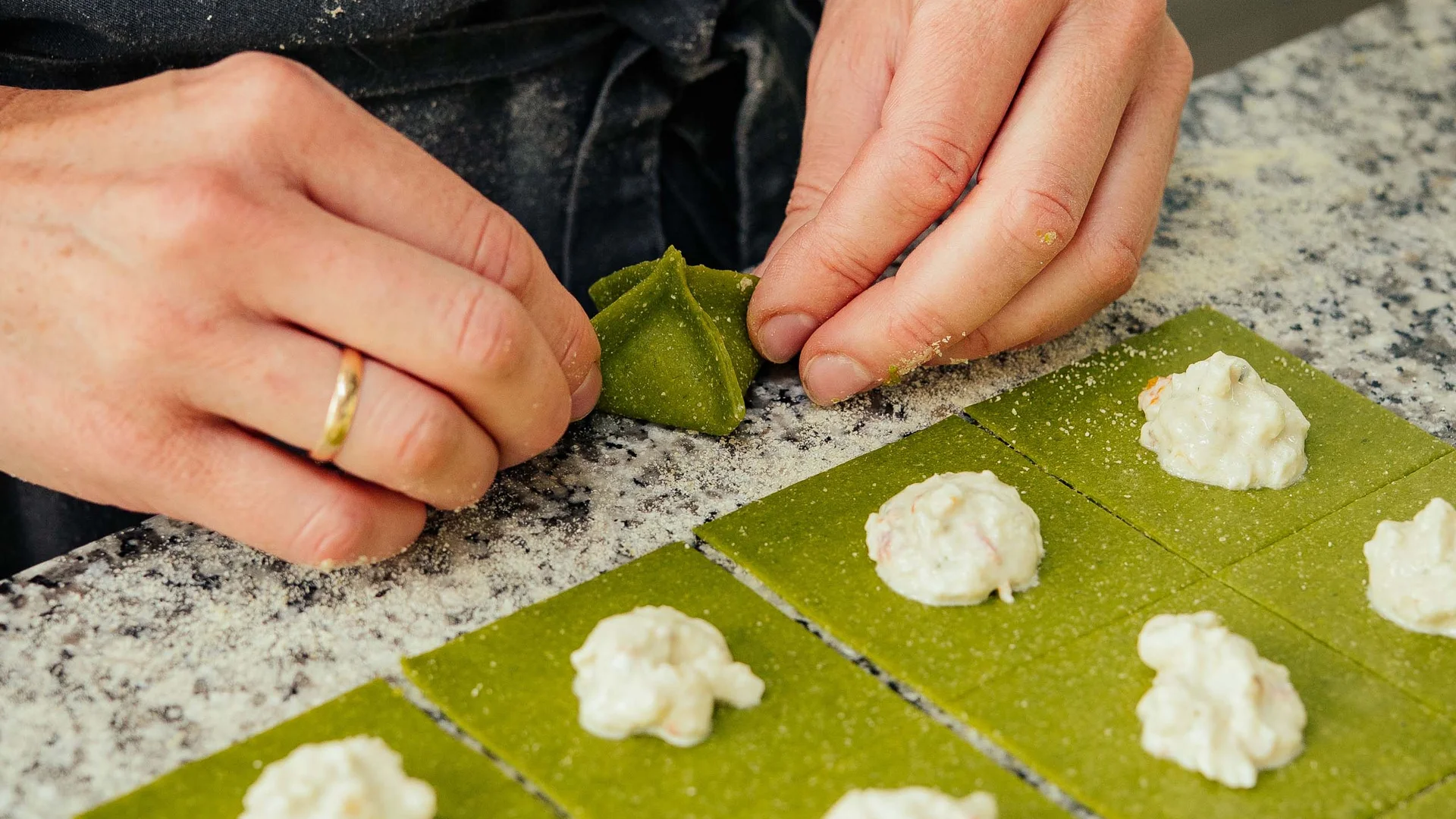 Mani che modellano quadrati di pasta verde con ripieno bianco
