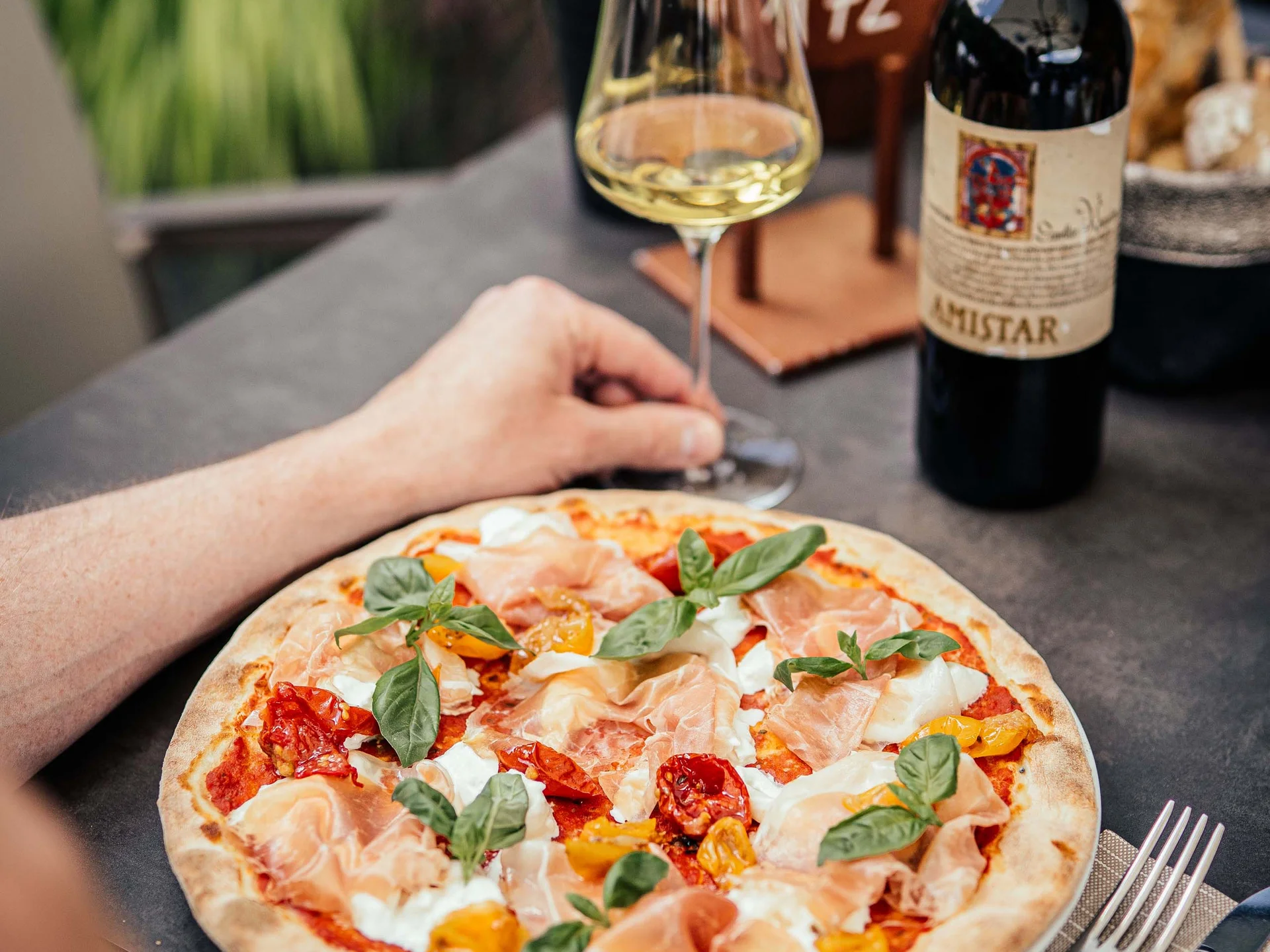 Der Lodenwirt in Vintl | Hotel, Residence & Restaurant Pizza mit Prosciutto, Basilikum und Tomaten, Glas Weißwein und Weinflasche