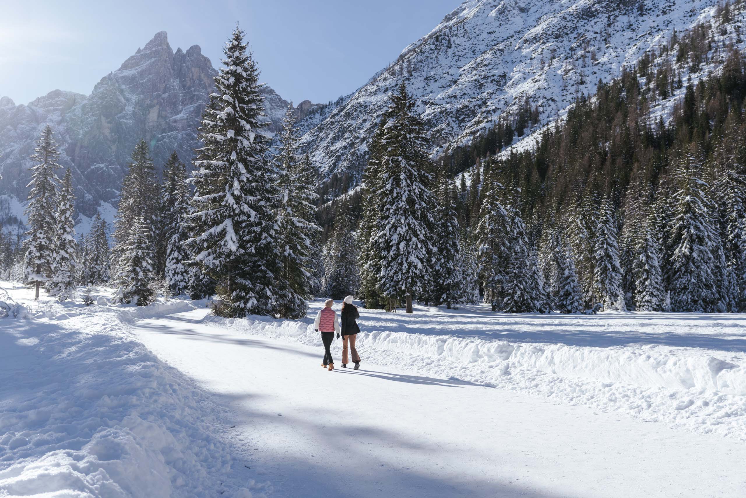 Due persone camminano in un bosco innevato ai piedi di montagne coperte di neve