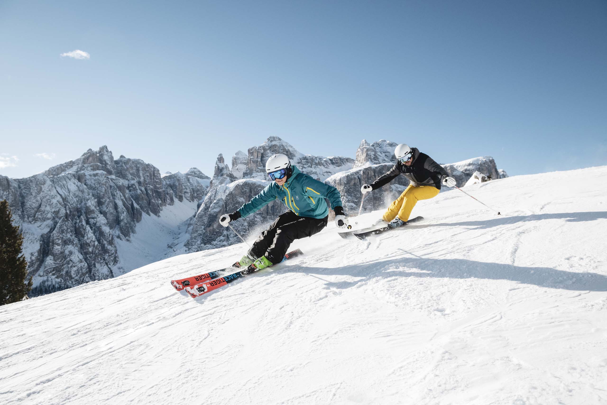 Due sciatori scendono lungo una pista innevata davanti a cime montuose
