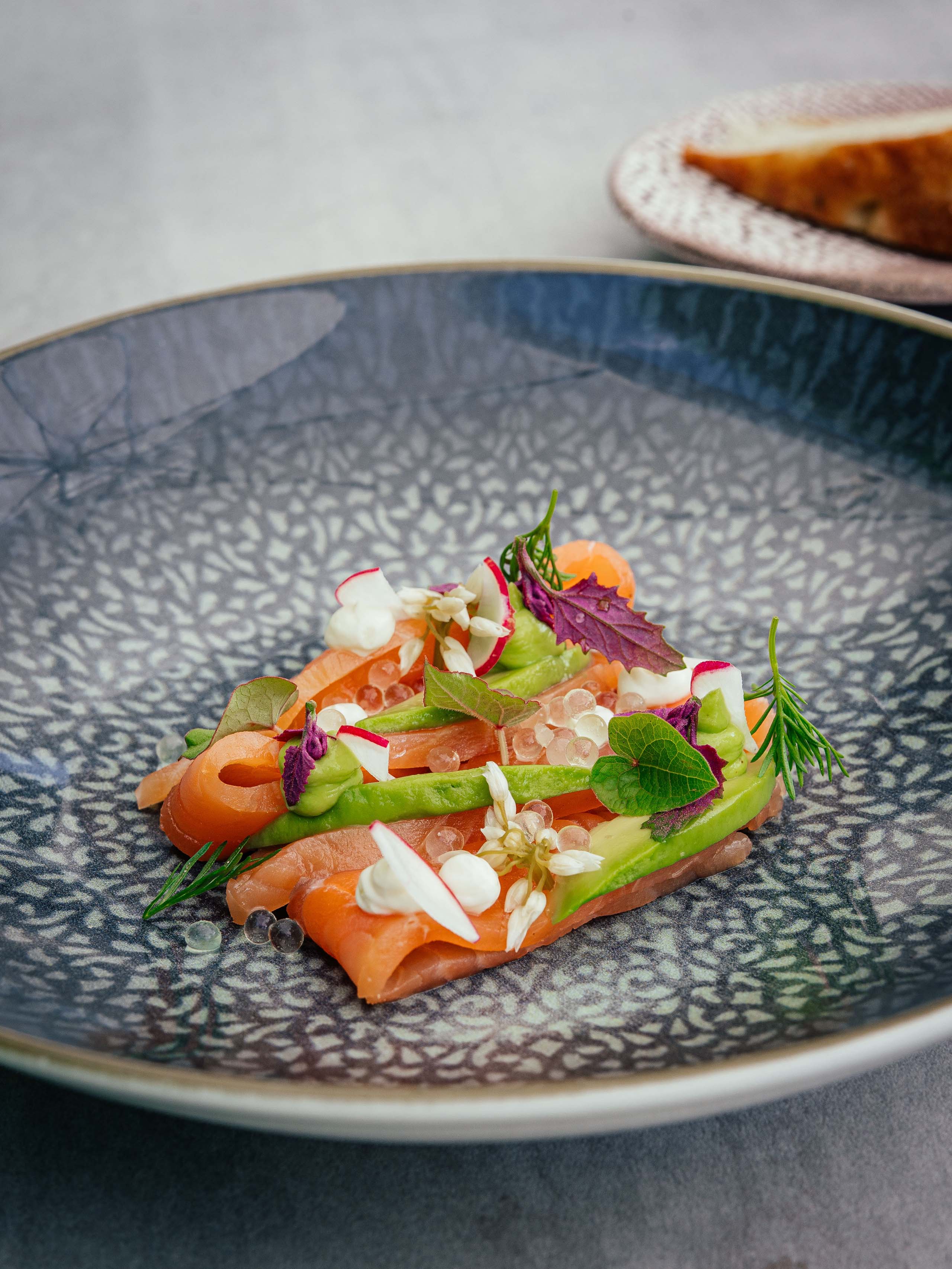 Il Lodenwirt a Vandoies | Hotel, residence e ristorante Salmone finemente decorata con erbe e fiori commestibili su piatto blu