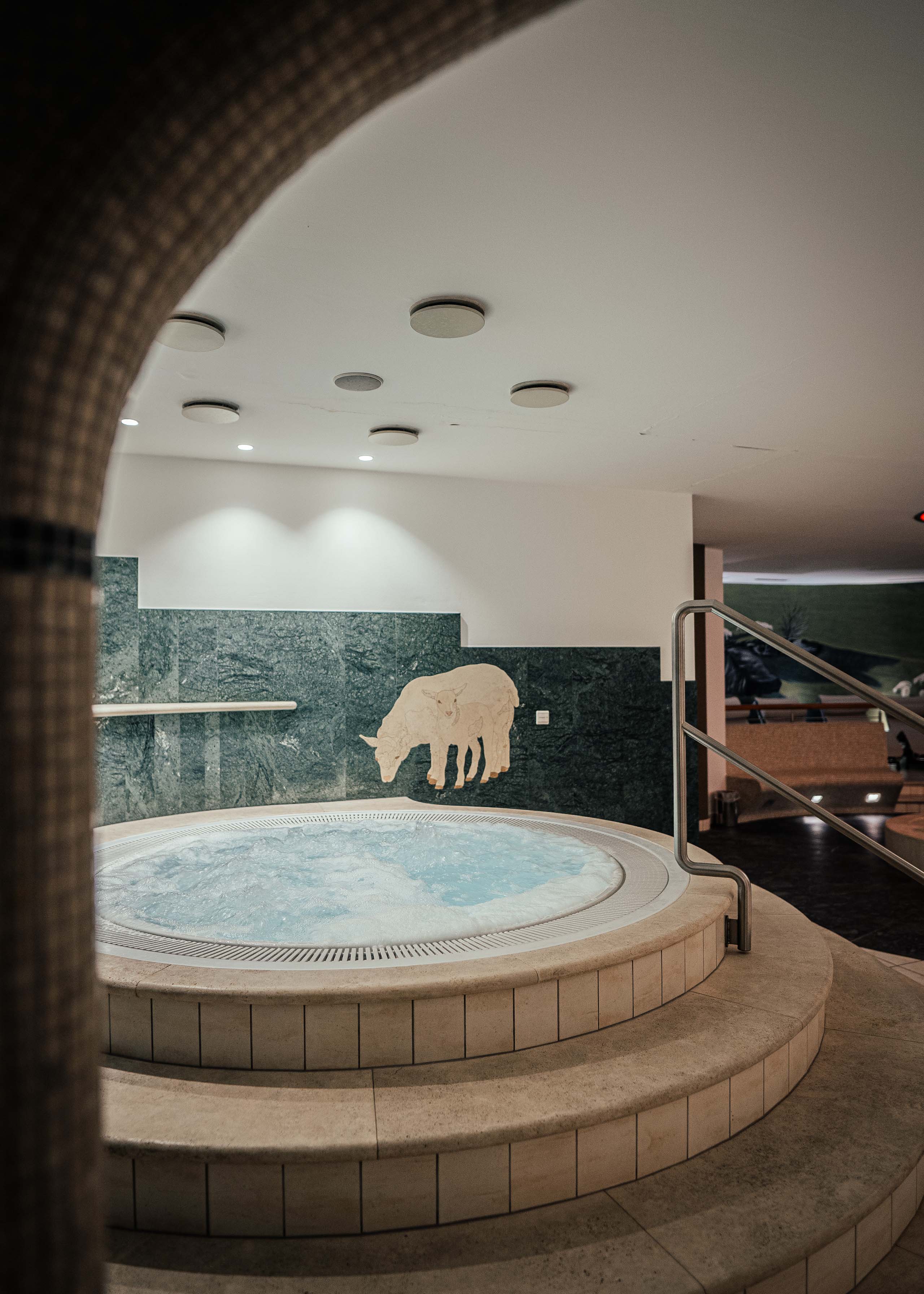 Your hotel with sauna in Val Pusteria/Pustertal Round hot tub with steps and a relief of a cow on a green wall in an indoor setting